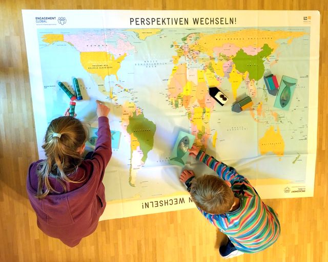 Weltkarte auf dem Boden mit 2 darauf knieenden Kindern