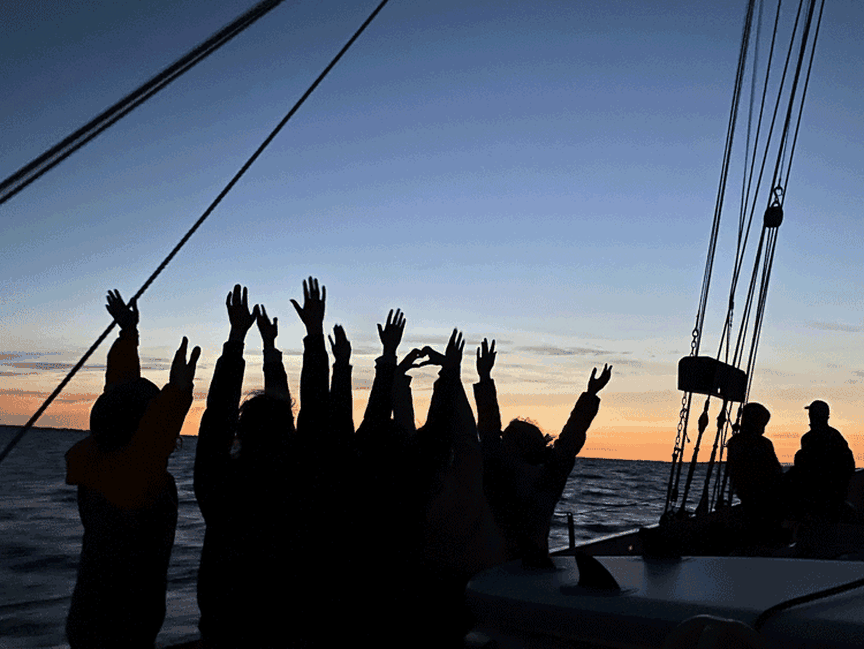 Menschen stehen bei Abendstimmung an Deck eines Segelschiffes