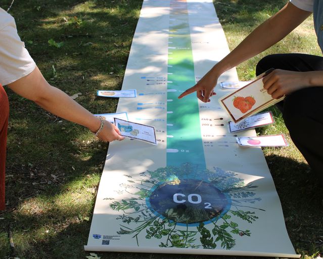 Auf dem Rasen liegende Plane mit 2 Personen davor knieend
