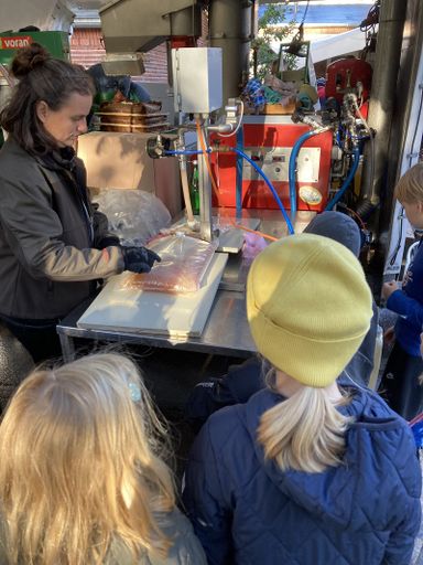 Eine Person verschließt ein Paket, 2 Kinder schauen zu.
