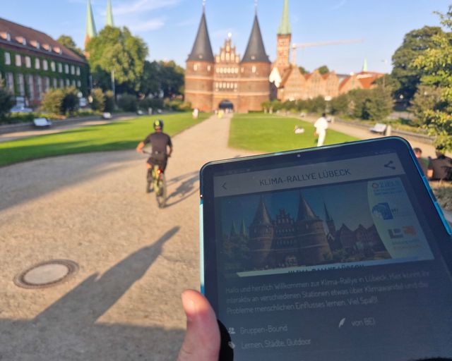 Holstentor im Hintergrund und vorne gehaltenes Tablet mit Holstentor in der Anzeige