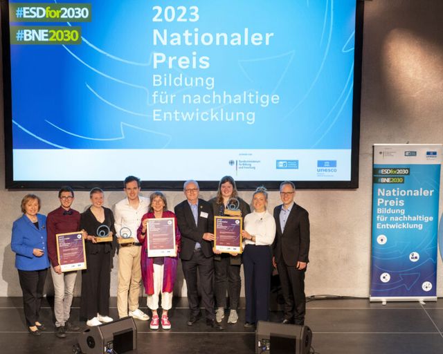 9 Personen stehen auf einer Bühne bei Preisverleihung