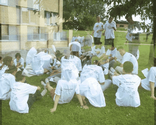 Zahlreiche Schüler_innen sitzen in einer Gruppe auf dem Rasen